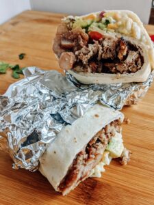 Carnitas burrito with queso, jalapeño pinto beans, and all the fixings! So delicious and easy to make ahead and freeze for another lunch or dinner.