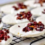 Close up of dried cranberry on top of white chocolate on top of cookie on a cooling rack.